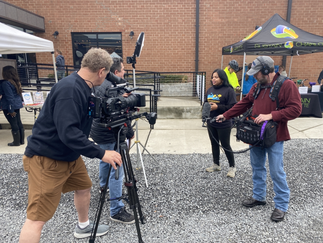 Camera operator and sound recordist filming an on-location interview at an outdoor community event